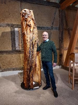 Man sieht Bernhard Schmid mit einer großen Holzskulptur